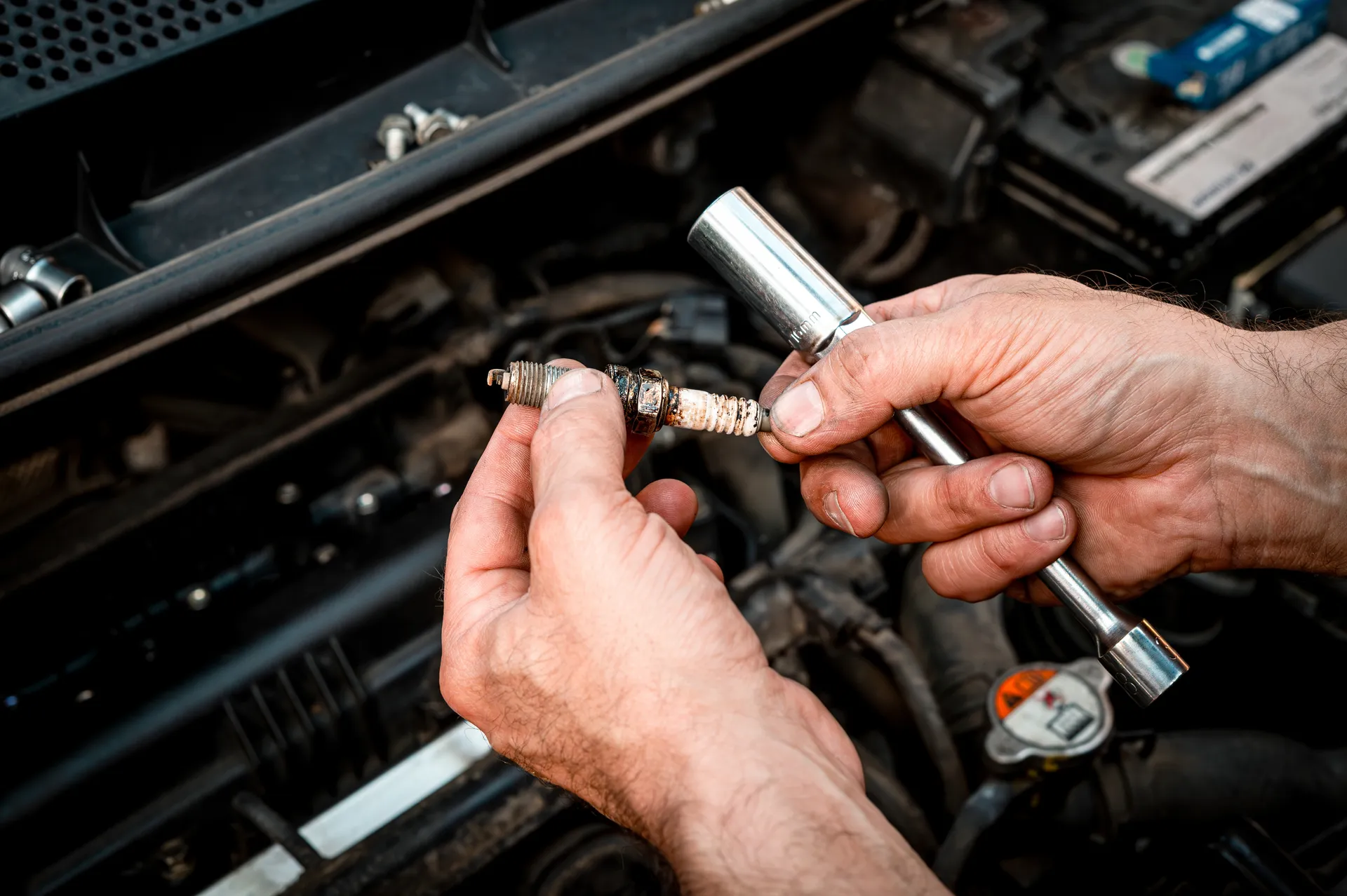 Mechanic holding a used spark plug and socket wrench during engine maintenance