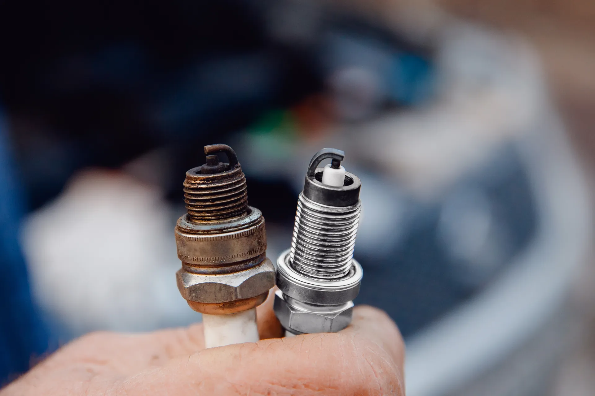Old and new spark plugs compared during vehicle maintenance