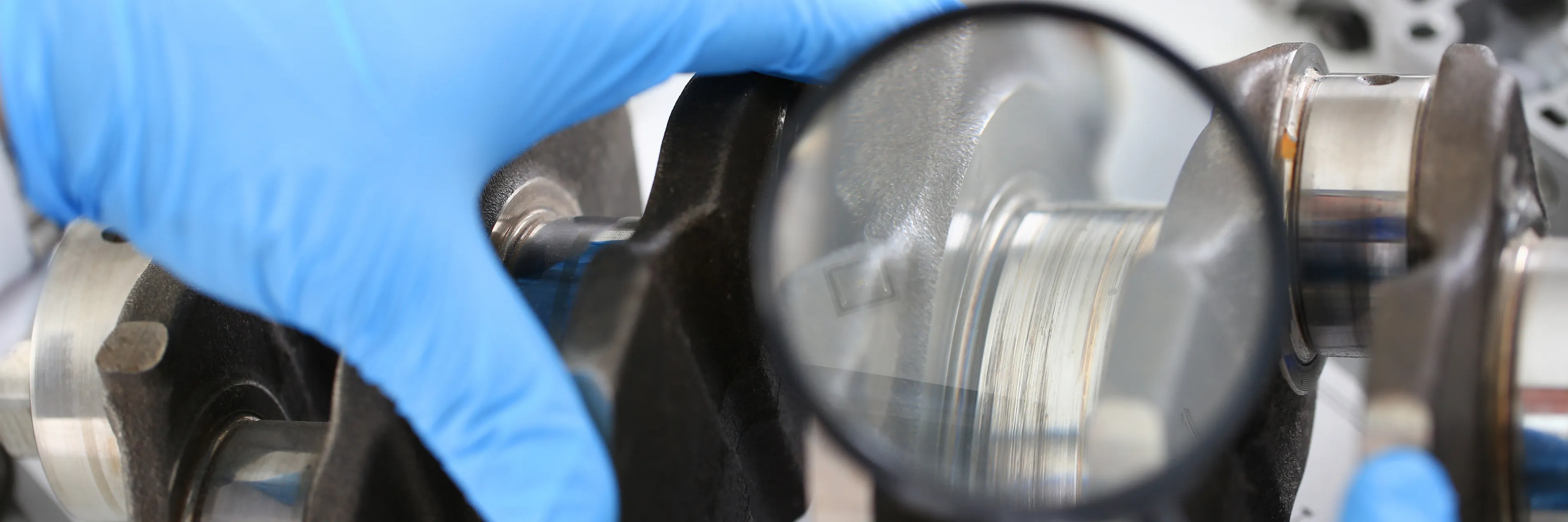 Technician inspecting a crankshaft surface with a magnifying glass.